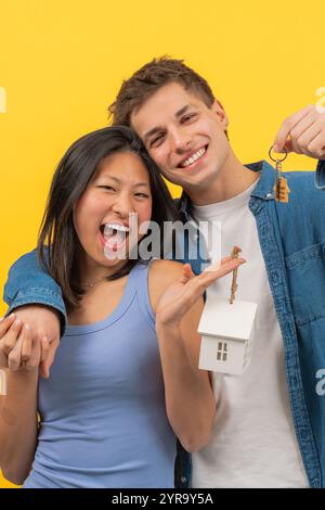 Coppia felice che tiene in mano le chiavi di casa e una piccola casa modello, per celebrare la nuova casa Foto Stock