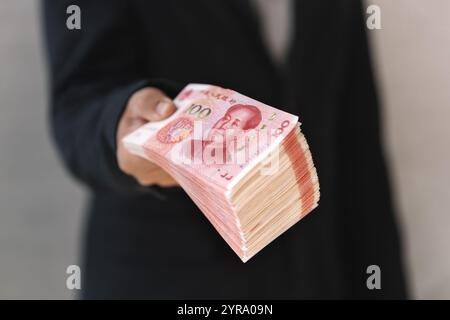 Le mani di una persona che ti propone dei soldi... primo piano. Un uomo tiene in mano lo yuan cinese. Il capo paga lo stipendio. Il concetto di corruzione e corr Foto Stock