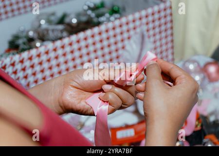 Primo piano delle mani di una donna che lega un nastro a una confezione regalo per la sua famiglia Foto Stock