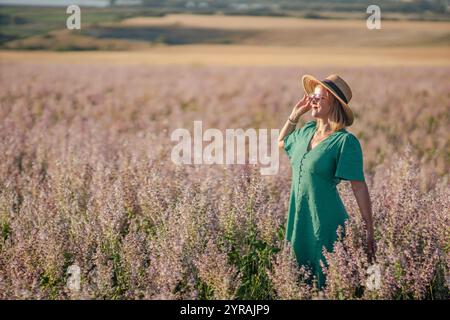 Woman Field Flowers: Happy Woman gode di un tramonto estivo in un campo fiorito; tranquilla scena naturale. Foto Stock