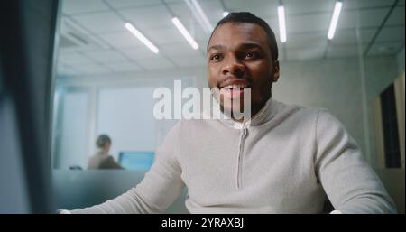 Un giovane uomo d'affari entusiasta si rallegra e celebra il successo dell'affare con il cliente, utilizza il computer, parla con il telefono cellulare. Specialista marketing afroamericano lavora in uffici moderni. E-commerce Foto Stock