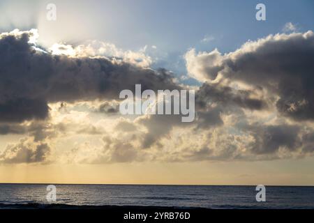 Alba mozzafiato con il sole che si nasconde dietro le nuvole, le onde del mare e il cielo blu con spazio fotocopie Foto Stock