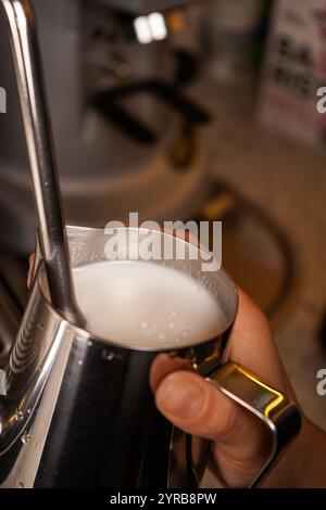 Un barista cuoce il latte in una caraffa utilizzando una macchina da caffè professionale, una macchina per cappuccino in un caffè. Foto Stock