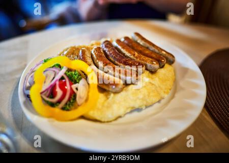 Un delizioso piatto di salsicce tedesche servito su un letto di crema di patate, guarnite con verdure fresche, tra cui lattuga, cipolla e campana Foto Stock