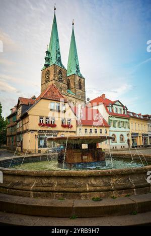 Una scena pittoresca caratterizzata da un edificio storico a Quedlinburg, in Germania, con guglie gemelle e una fontana in primo piano, che mostra un tradizionale a Foto Stock