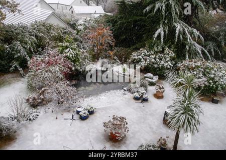Giardino con neve fitta, laghetto ghiacciato, piante innevate, arbusti e alberi a Sidmouth, Devon, Regno Unito Foto Stock