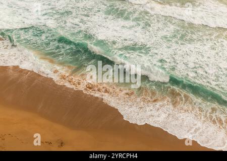 Vista aerea delle onde che si infrangono su una spiaggia sabbiosa lungo la Great Ocean Road in Australia. Le impronte attraversano la sabbia, aggiungendo un tocco umano al Foto Stock