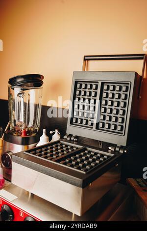 Superficie per friggere waffle belgi. Forma per i waffle. Bollitore elettrico per waffle su un tavolo di legno. Primo piano in una caffetteria Foto Stock