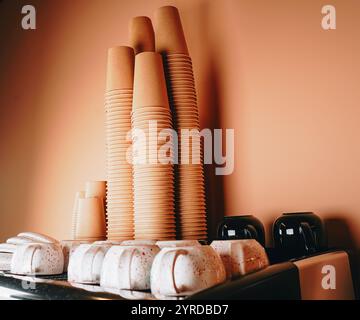 Un gruppo di tazze di carta si siede sulla macchina del caffè e le loro stampe vivaci aggiungono un tocco di colore all'elegante e moderno allestimento del caffè Foto Stock