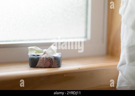 Sapone al carbone fatto a mano avvolto in nastro di tessuto su un davanzale in legno Foto Stock