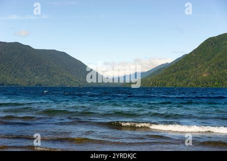 Vista panoramica di un tranquillo lago circondato da montagne boschive in un giorno di sole Foto Stock