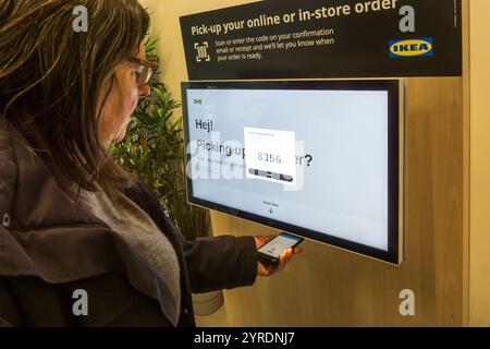 Donna che consente a un terminale di un negozio IKEA di leggere un codice a barre sul suo cellulare per ritirare un ordine online. Foto Stock