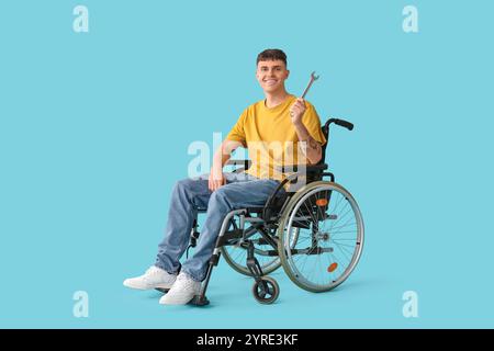 Bellissimo giovane uomo felice con chiave che ripara sedia a rotelle su sfondo blu Foto Stock