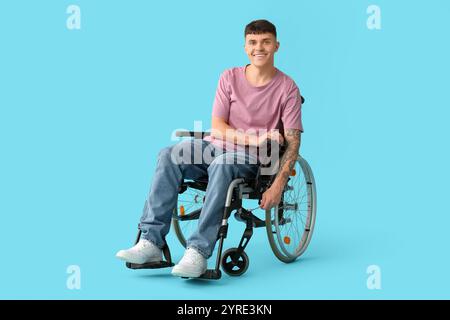 Bellissimo giovane uomo felice con chiave che ripara sedia a rotelle su sfondo blu Foto Stock