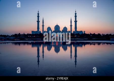 Grande Moschea dello Sceicco Zayed illuminata al crepuscolo con la sua serena riflessione sull'acqua, che mostra maestose cupole e minareti ad Abu Dhabi Foto Stock