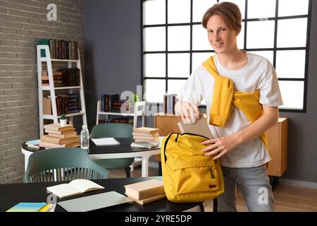 Studente di sesso maschile che mette il libro nello zaino della biblioteca Foto Stock