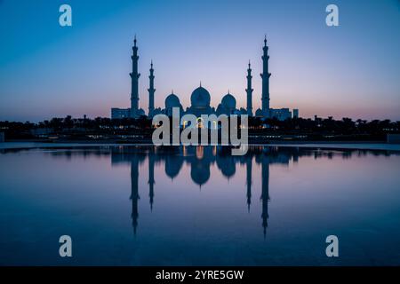 Grande Moschea dello Sceicco Zayed illuminata al crepuscolo con la sua serena riflessione sull'acqua, che mostra maestose cupole e minareti ad Abu Dhabi Foto Stock