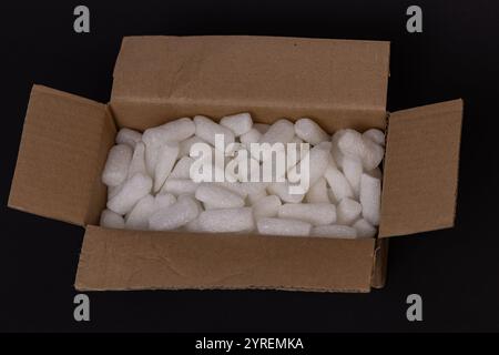 Scatola di cartone riempita con arachidi di imballaggio in schiuma bianca per un imballaggio e un trasporto sicuri su sfondo scuro Foto Stock