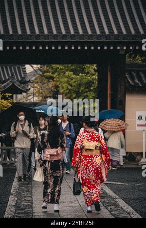 Le persone vestite con vivaci kimono tradizionali camminano graziosamente attraverso le strade storiche di Kyoto, in Giappone, circondate da fascino culturale. Foto Stock
