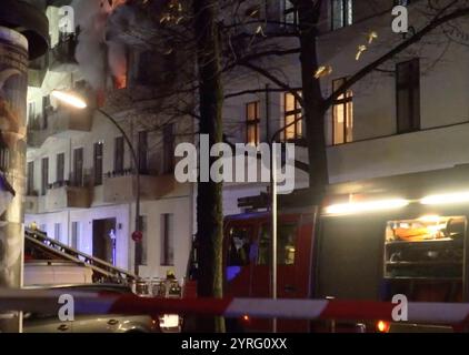 Berlino, Germania. 4 dicembre 2024. I vigili del fuoco lavorano su una finestra in fiamme in un condominio. Un incendio in un condominio a più piani ha innescato un'importante operazione notturna da parte dei servizi di emergenza di Berlino-Neukölln. Secondo i vigili del fuoco, hanno risposto 117 vigili del fuoco. (A dpa: "Oltre 100 servizi di emergenza combattono il fuoco a Neukölln") credito: Julius-Chrstian Schreiner/dpa/Alamy Live News Foto Stock