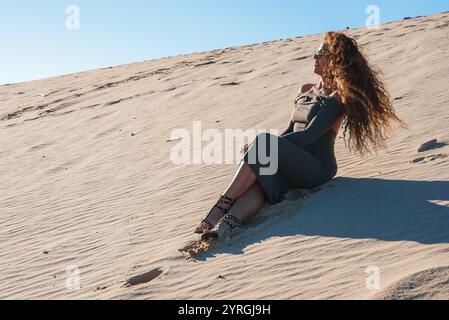 Donna seduta sulla duna di sabbia sotto cielo aperto a Tarifa, Spagna Foto Stock