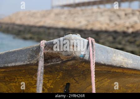 Una barca intemprata con funi rustiche ancorata sulla riva dell'isola di Qeshm, che mostra l'aspra bellezza della vita marittima tradizionale. Foto Stock