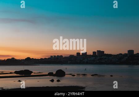 Il sole tramonta dipinge il cielo con vivaci sfumature di arancione e rosa sul fiume douro a vila nova de gaia, porto, portogallo, come sagome di buil Foto Stock