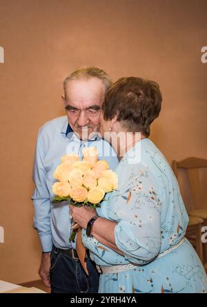 Senior russo 75 anni coppia celebrando il matrimonio d'oro e baciando la guancia nel registro del matrimonio, le iscrizioni russe delle loro medaglie dicono 50 Foto Stock