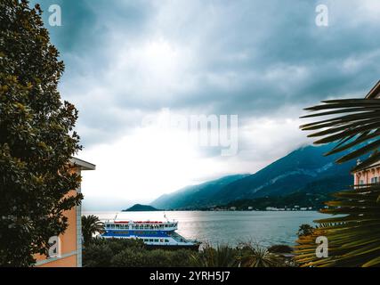 Attracco dei traghetti al molo di bellagio, un incantevole villaggio sul lago di como, in italia, circondato da montagne e sotto un cielo nuvoloso, creando un dramati Foto Stock