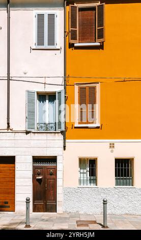 La luce del sole illumina la vibrante facciata di un edificio residenziale a parma, italia, che mette in mostra un mix di persiane aperte e chiuse, aggiungendo un tocco di fascino Foto Stock