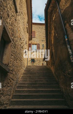 Vista ad angolo basso di una scala di pietra che sale tra edifici in pietra intemprata in uno stretto vicolo di san marino, con persiane marroni, uno scorcio Foto Stock