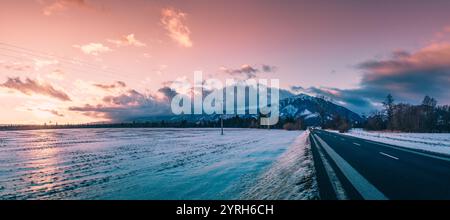 Paesaggio innevato con una strada asfaltata che conduce a krivan, alti tatra, slovacchia, durante un bellissimo tramonto invernale con nuvole rosa e viola. Foto Stock