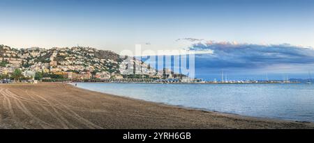 Vista panoramica delle rose, spagna, che mostra la città annidata su una collina, una spiaggia tranquilla e le barche ancorate nella baia durante un vibrante tramonto Foto Stock