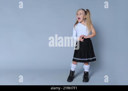 la giovane ragazza con i capelli biondi in coda si staglia su uno sfondo grigio, indossa un top bianco a maniche lunghe, una gonna a pieghe nere e un pizzo Foto Stock