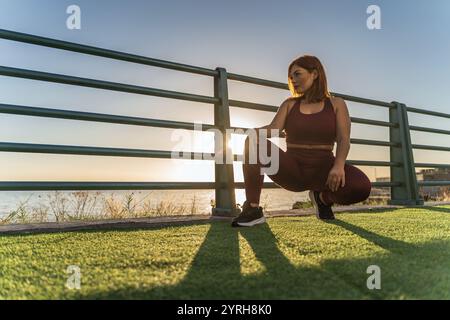 Una donna sportiva più grande che si prende una pausa in mare durante la routine di fitness al tramonto Foto Stock