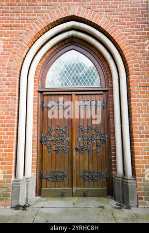 Vecchia porta di una chiesa europea con un arco rotondo. Ingresso antico in legno e decorazioni metalliche. Foto Stock