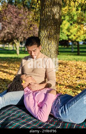 Una coppia gode di una serena giornata autunnale in un parco, seduto sotto un albero con una coperta spalmata il terreno è ricoperto di foglie gialle, aggiungendo calore al suo interno Foto Stock