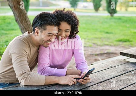 Una coppia gioiosa si siede vicino a un tavolo da picnic, condividendo una risata mentre guarda uno smartphone in un parco panoramico la vibrante vegetazione li circonda, creato Foto Stock