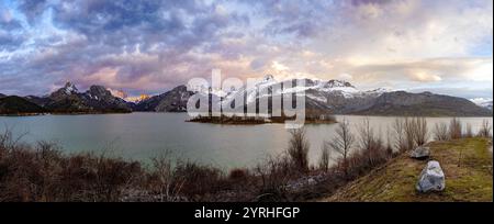 Uno splendido tramonto illumina le montagne innevate accanto a un lago sereno, la scena cattura un'atmosfera tranquilla con nuvole colorate e riflessi tranquilli Foto Stock