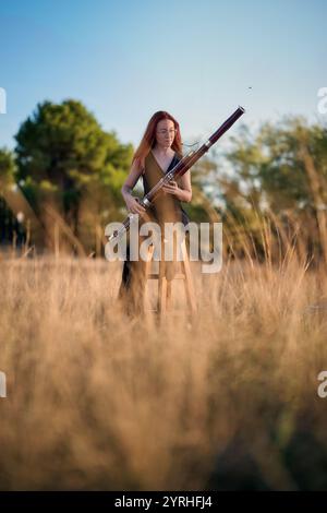Una donna siede su uno sgabello che suona un fagotto in un campo sereno la luce del sole dorata filtra attraverso l'erba alta, creando un ambiente musicale suggestivo e tranquillo Foto Stock