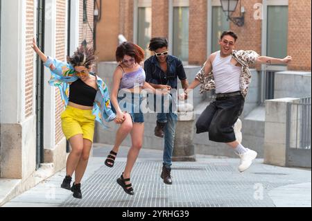 Un vivace gruppo di quattro amici che saltano gioiosamente in un'atmosfera urbana, dimostrando un momento spensierato pieno di risate ed energia. Foto Stock