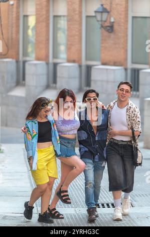 Un allegro gruppo di quattro amici che ridono e camminano per una strada della città, mostrando i loro stili di moda unici con abiti estivi luminosi. Foto Stock