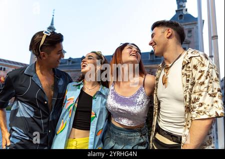 Un vivace gruppo di quattro amici che condividono un momento di gioia in una strada cittadina, ridendo e godendosi la compagnia reciproca, vestiti colorati e alla moda Foto Stock