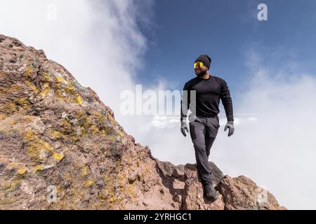 Un escursionista si erge con sicurezza sulla cima rocciosa del vulcano la Malinche in Messico, circondato da spettacolari nuvole e cielo, perfetto per temi di avventura Foto Stock