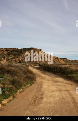 Esplora l'arida bellezza delle Bardenas Reales a Navarra, in Spagna, Una tortuosa strada sterrata conduce attraverso aspre colline scolpite sotto un vasto cielo, mostrando nat Foto Stock