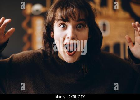 Una giovane donna con un'espressione sorpresa, la bocca aperta e gli occhi spalancati. Si trova su uno sfondo sfocato, catturando un momento di eccitazione o. Foto Stock