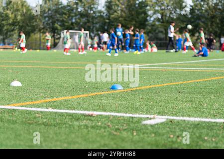 Una vivace sessione di allenamento di calcio giovanile si svolge su un lussureggiante campo verde, con giovani giocatori che praticano con entusiasmo coni di allenamento e pali Foto Stock