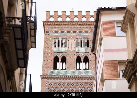 L'immagine mostra l'imponente torre mudejar di El Salvador a Teruel, adornata da intricati disegni di piastrelle, incorniciata da edifici moderni, che mettono in risalto la t Foto Stock