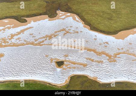 Vista aerea che mostra la costa meridionale dell'Islanda, evidenziando intricati schemi di zone umide che si fondono con lussureggianti campi verdi, creando uno splendido ambiente naturale Foto Stock