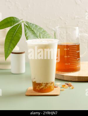 Un rinfrescante tè al latte freddo condito con panna spalmata, servito in una tazza trasparente di gelatina d'ambra poggia sul fondo, accompagnato da un bicchiere di tè estratto su una Foto Stock